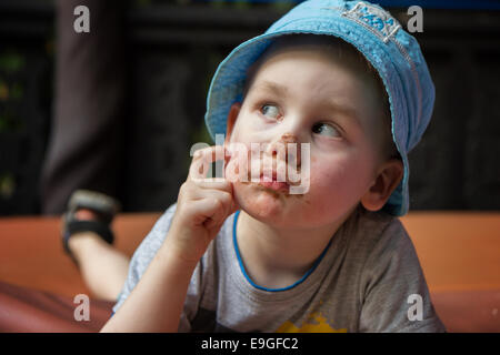 Primo piano di un piccolo ragazzo ponderando, faccia macchiata con il cioccolato Foto Stock