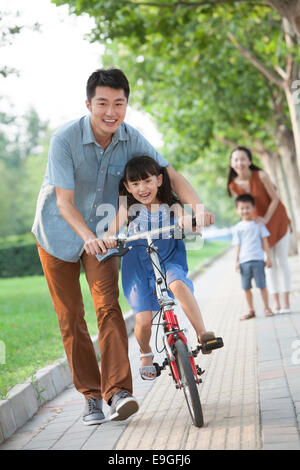 Giovane padre ad insegnare la sua figlia ad andare in bicicletta Foto Stock