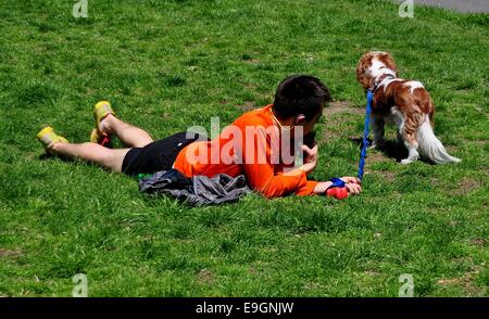 NYC: giovane uomo con il suo cane si rilassa sul centro di Prato mediano in Riverside Park in un assolato pomeriggio di primavera Foto Stock