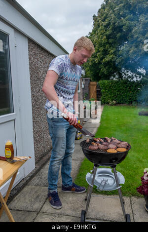 Giovani maschi adulti cercando di luce di un barbecue e di cottura degli alimenti in estate Foto Stock