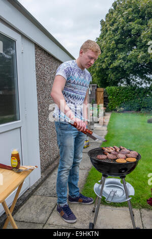 Giovani maschi adulti cercando di luce di un barbecue e di cottura degli alimenti in estate Foto Stock