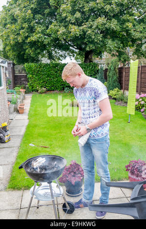 Giovani maschi adulti cercando di luce di un barbecue in estate Foto Stock