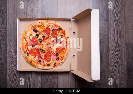 La pizza italiana con prosciutto, pomodori e olive in scatola, su grigio sfondo tabella Foto Stock