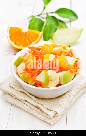 Frutta Ortaggi con Insalata di carote, mele, banane e fettine di arancia in una terrina bianco sul tavolo di legno Foto Stock