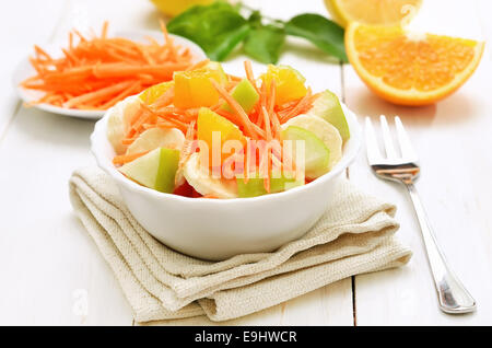 Frutta con Insalata di carote, mele, banane e fettine di arancia in una terrina bianco sul tavolo di legno Foto Stock