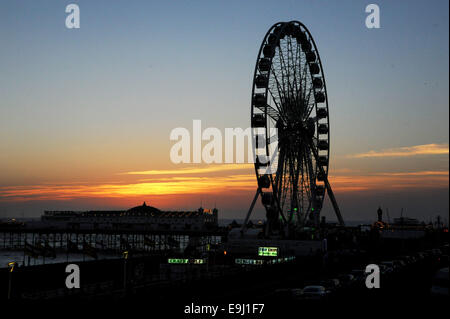 Il sole tramonta dietro la ruota di eccellenza sul lungomare di Brighton come le persone prendono un inizio serata ride dopo una calda giornata di sole Foto Stock