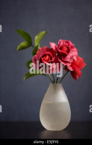 Un trio di mute rose rosse in un semplice vaso di vetro. Foto Stock