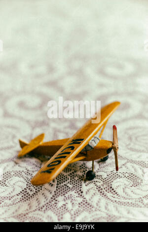 Un antico legno giallo aeroplano giocattolo siede su un pizzo coperto il piano portapaziente. Foto Stock