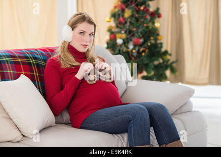 Sorridente donna incinta con scarpe per bambini sul suo ventre Foto Stock