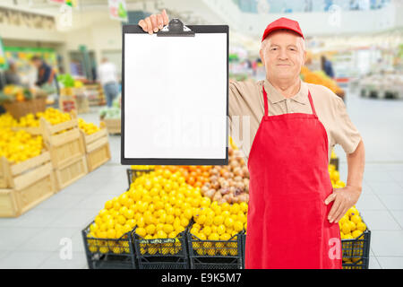 Mercato maturo fornitore tenendo un clipboard di fronte un corridoio con frutta e verdura Foto Stock