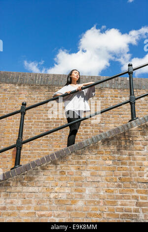 Basso angolo vista della giovane donna che guarda lontano mentre appoggiata sulla ringhiera contro il cielo nuvoloso Foto Stock