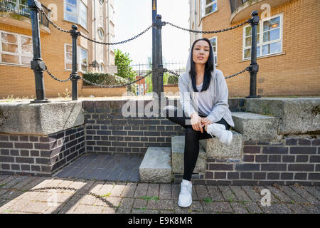A piena lunghezza Ritratto di fiducioso giovane donna seduta su scale contro la costruzione di Foto Stock