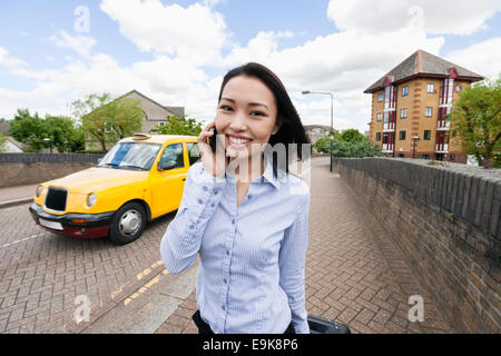 Ritratto di sorridere imprenditrice risposta cellulare sul marciapiede con il taxi in background Foto Stock