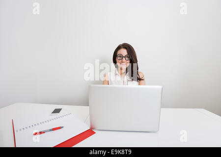 Ritratto di giovane imprenditrice in nerd occhiali con computer portatile alla scrivania in ufficio Foto Stock