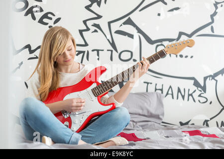 Lunghezza intera della ragazza adolescente a suonare la chitarra in camera da letto Foto Stock