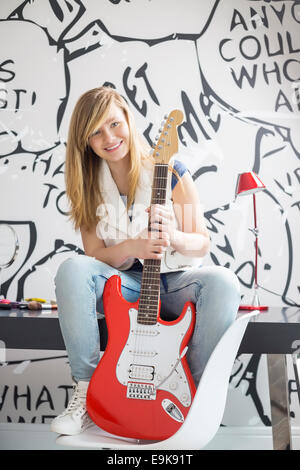 Ritratto a figura intera della ragazza adolescente con chitarra elettrica seduto sul tavolo da studio a casa Foto Stock