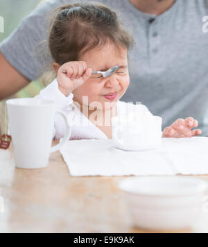 Ragazza carina rendendo faccia mentre avente la crema con il padre a casa Foto Stock