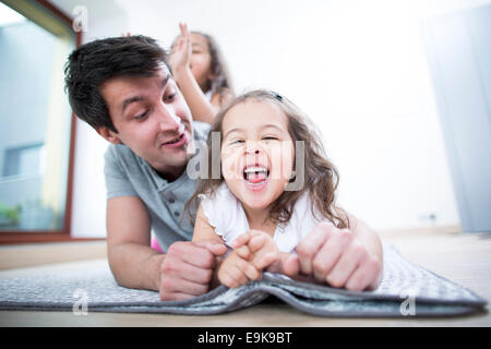 Padre guardando allegro figlia giacente su una coperta a casa Foto Stock