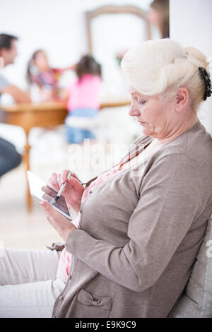 Vista laterale della donna senior con tavoletta digitale in casa Foto Stock