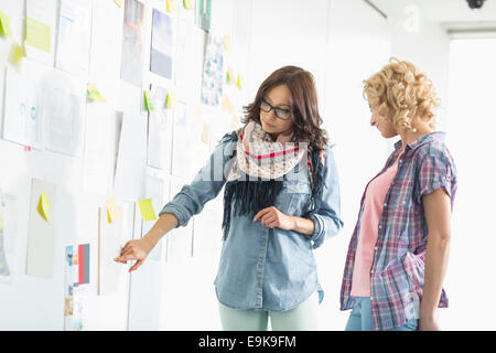 Imprenditrici discutendo su carte bloccato sulla parete in ufficio creativo Foto Stock