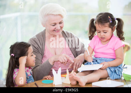 Felice donna senior assistere nipoti nel rendere l'artigianato a casa Foto Stock