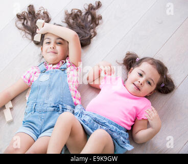 Angolo di alta vista di carino piccole sorelle sdraiato sul pavimento in legno a casa Foto Stock