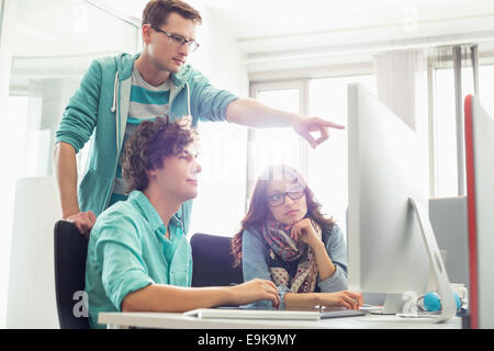 Imprenditore mostrando qualcosa ai colleghi sul computer in ufficio creativo Foto Stock