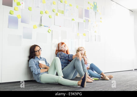 Stanco imprenditrici seduto sul pavimento in ufficio creativo Foto Stock