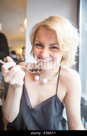 Ritratto di felice giovane donna mangiare pasticcini al cafe Foto Stock