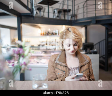 Felice giovane donna la lettura di un messaggio di testo sul telefono cellulare in cafe Foto Stock