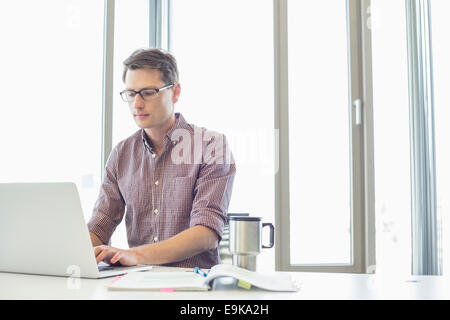 Imprenditore lavora su computer portatile alla scrivania in ufficio creativo Foto Stock