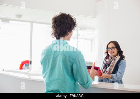 Felice imprenditrice dando file al collega di sesso maschile a contatore in ufficio creativo Foto Stock