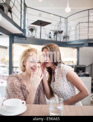 Ritratto di giovane donna whispering in femmine di amico del orecchio in cafe Foto Stock