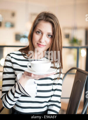 Ritratto di giovane donna azienda tazza da caffè con piattino al cafe Foto Stock