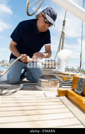 Uomo di mezza età winching fune su yacht Foto Stock