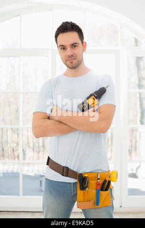 Ritratto di fiducioso uomo con trapano a mano nella nuova casa Foto Stock