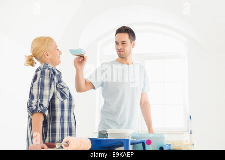 Giocoso uomo mettendo la vernice sulla donna di naso nella nuova casa Foto Stock