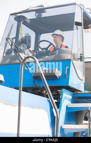 Lavoratore di sesso femminile che di funzionamento del carrello elevatore a forche in cantiere di spedizione Foto Stock