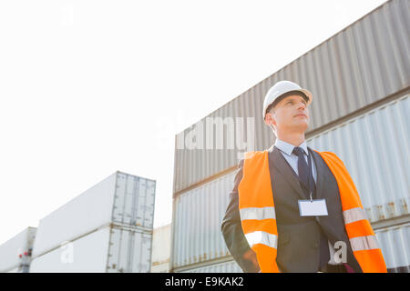 Basso angolo vista del lavoratore in piedi contro il container in cantiere di spedizione Foto Stock