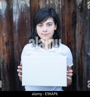 Teen ragazza con un foglio bianco nelle sue mani, una vecchia parete in legno sullo sfondo. Foto Stock