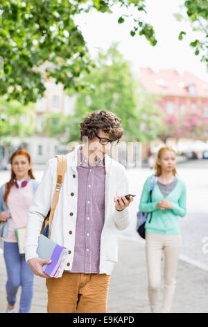 Giovani studenti di sesso maschile mediante telefono cellulare con amici in background su strada