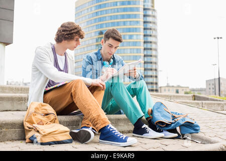 Lunghezza completa di maschi giovani studenti universitari che studiano sui gradini contro un edificio Foto Stock