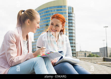 Sorridente giovani studenti universitari che studiano contro la costruzione di Foto Stock