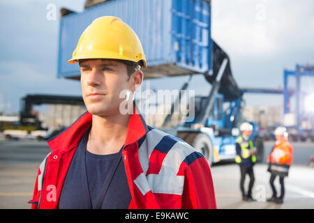 Fiducioso lavoratore di sesso maschile con i colleghi in background in cantiere di spedizione Foto Stock