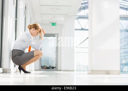 A tutta lunghezza laterale di sottolineato imprenditrice accovacciato in ufficio corridoio Foto Stock