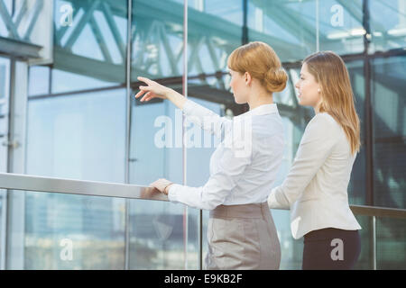 Imprenditrice mostrando qualcosa al collega di sesso femminile da parete in vetro in office Foto Stock