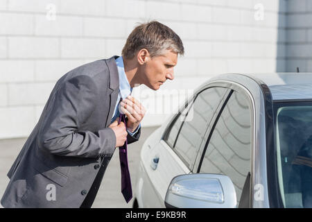 Vista laterale di imprenditore tirante di regolazione mentre la ricerca nella finestra auto Foto Stock