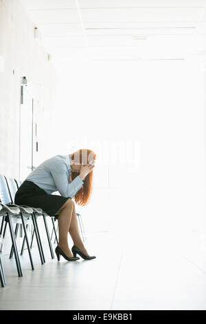 Vista laterale del frustrato imprenditrice seduti su una sedia in ufficio Foto Stock