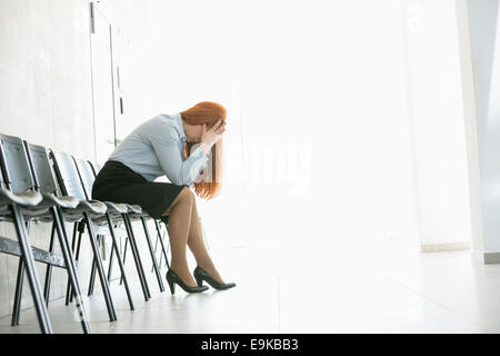 Vista laterale di esaurito imprenditrice seduti su una sedia in ufficio Foto Stock