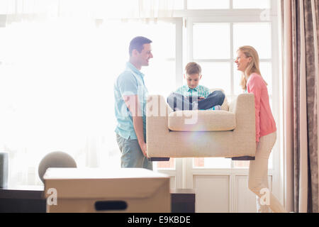 Genitori felici che trasportano figlio sulla poltrona nella nuova casa Foto Stock